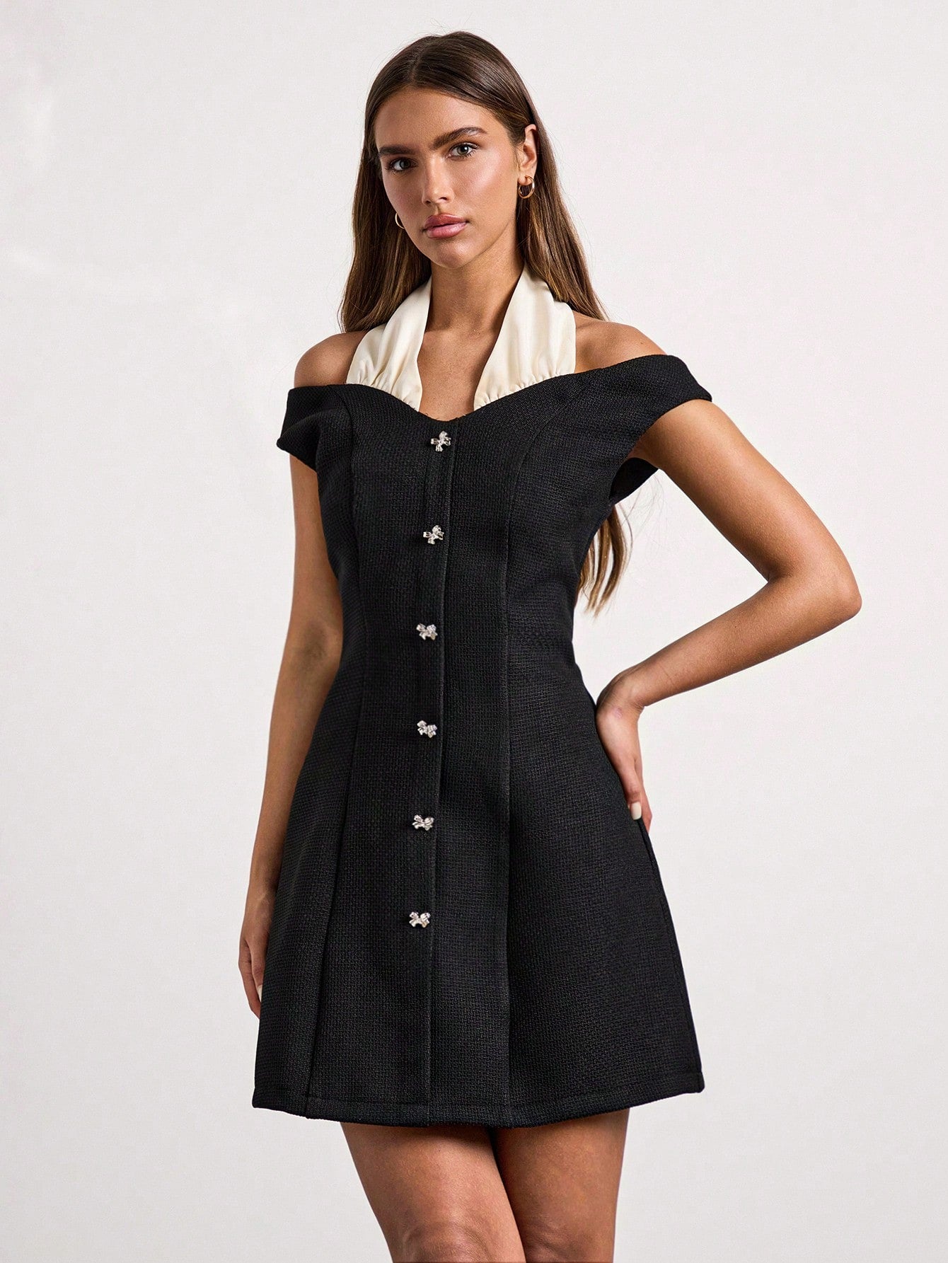 Woman wearing a black off-shoulder dress with a white scarf on a light gray background