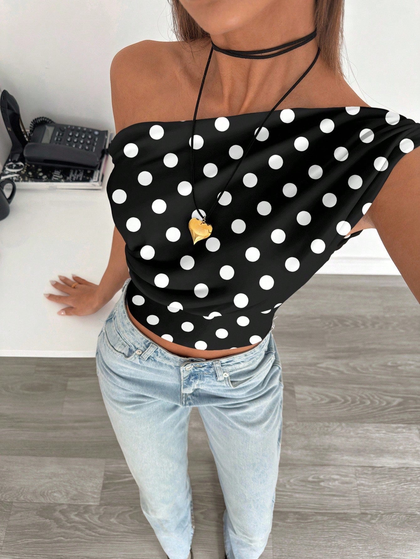 Person wearing a black polka dot top and light blue jeans indoors.