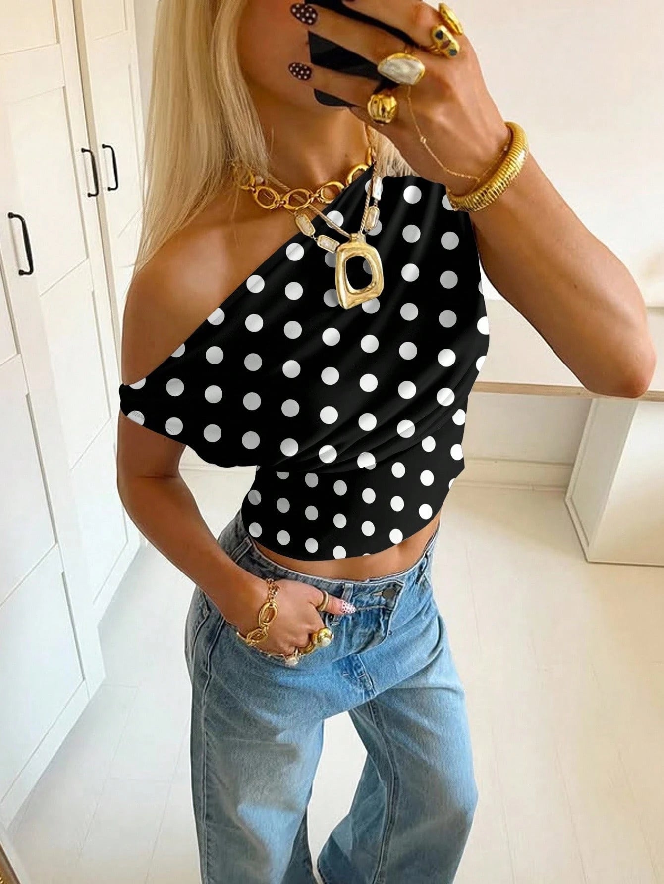 Person wearing a black polka dot top and blue jeans indoors.