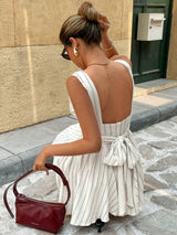 Woman in a white dress with a red handbag on a stone pavement.