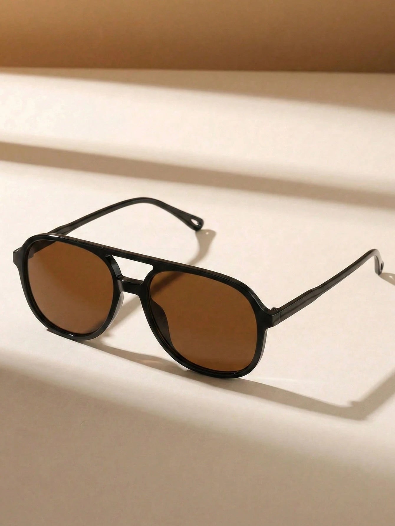 Black sunglasses with brown lenses on a beige background