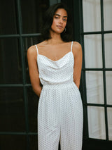 Woman wearing a white polka dot jumpsuit standing in front of a window.