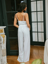 Woman wearing a white patterned jumpsuit standing in a room with a decorative fireplace.