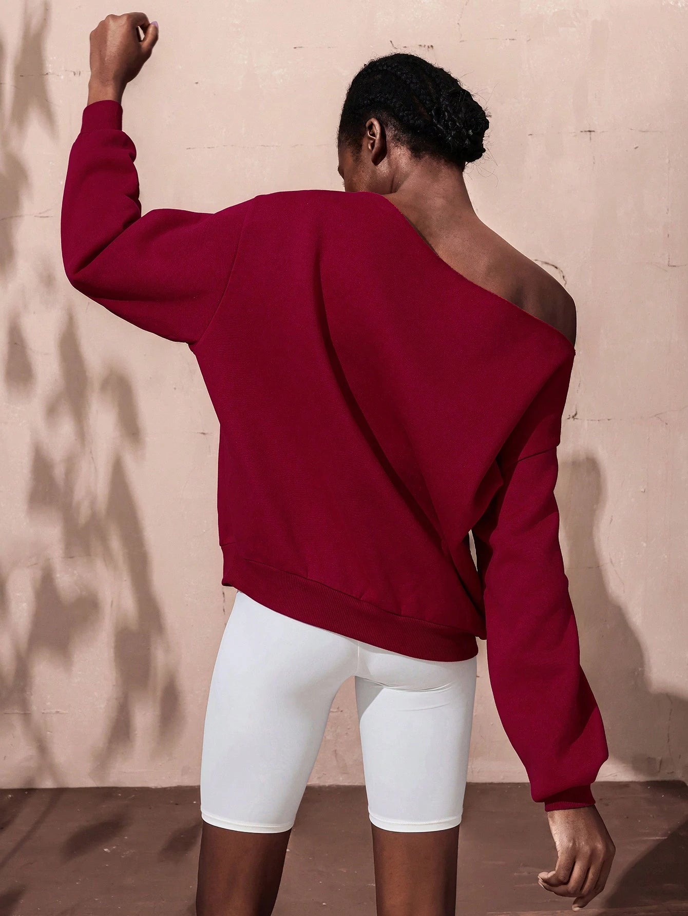 Person wearing a red hoodie and white shorts against a beige wall.