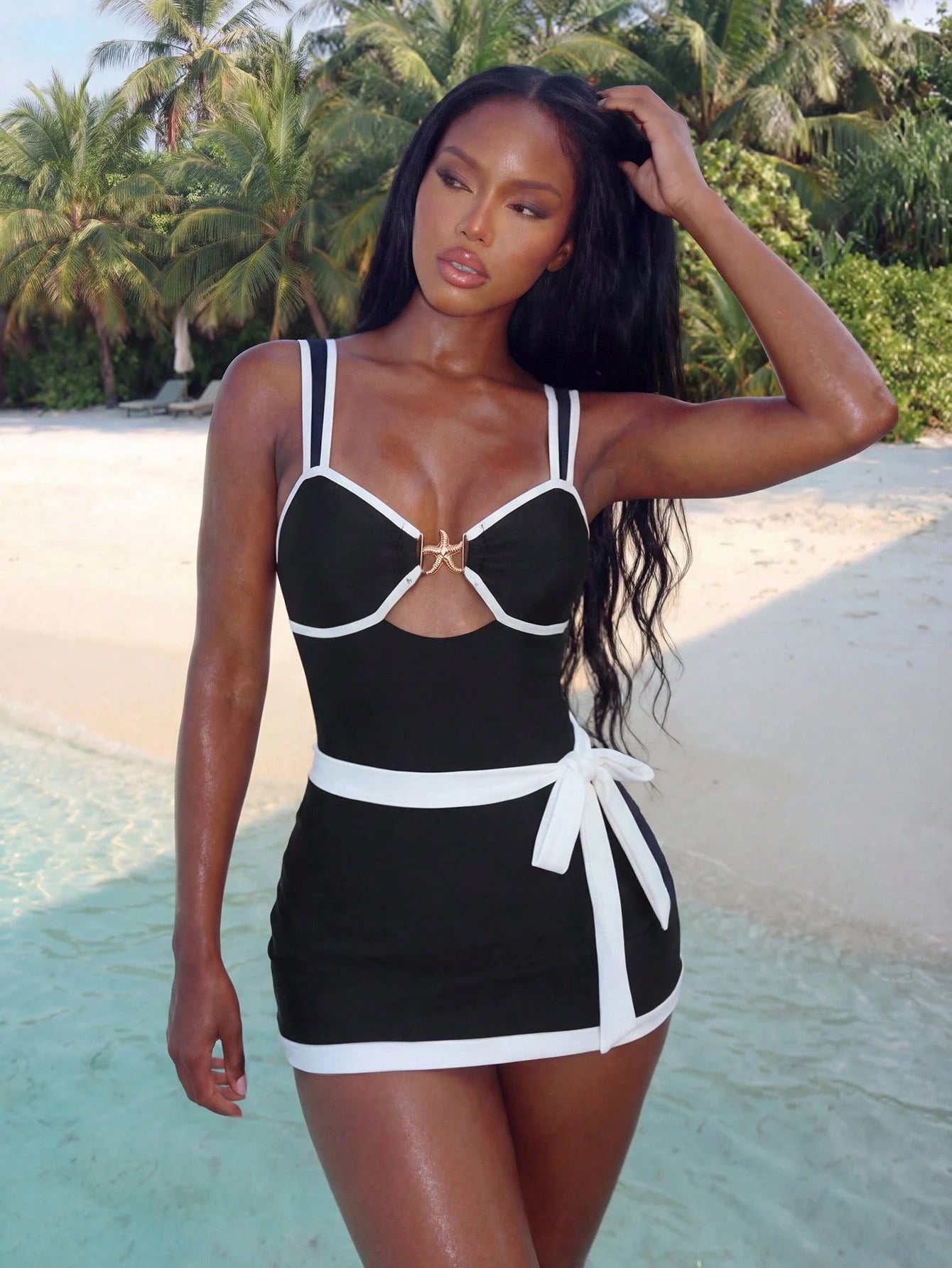 Woman in a black and white swimsuit standing on a beach with palm trees in the background