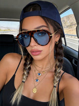 Woman wearing sunglasses and a cap inside a car with a scenic background