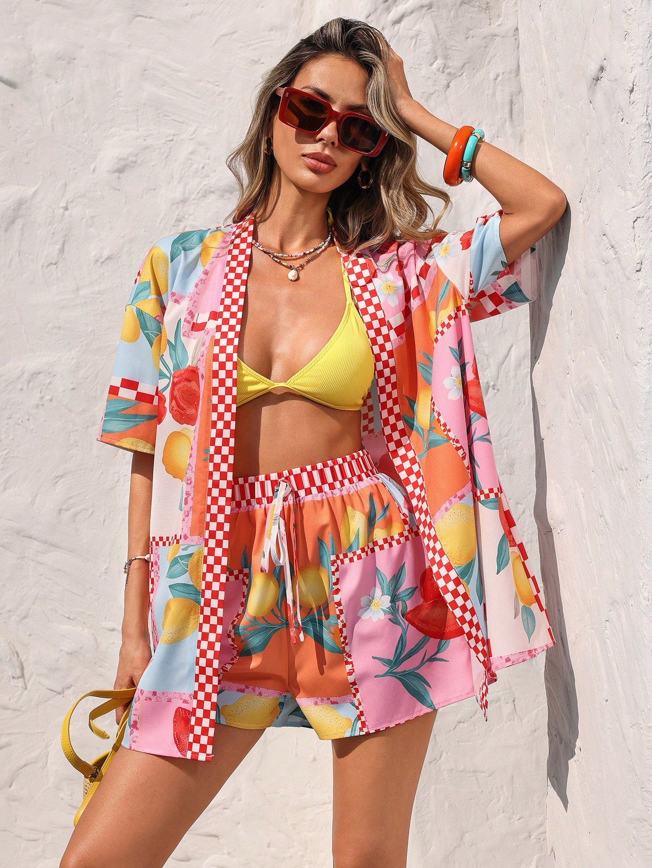 Woman wearing a colorful beach outfit with a kimono-style cover-up against a white wall.