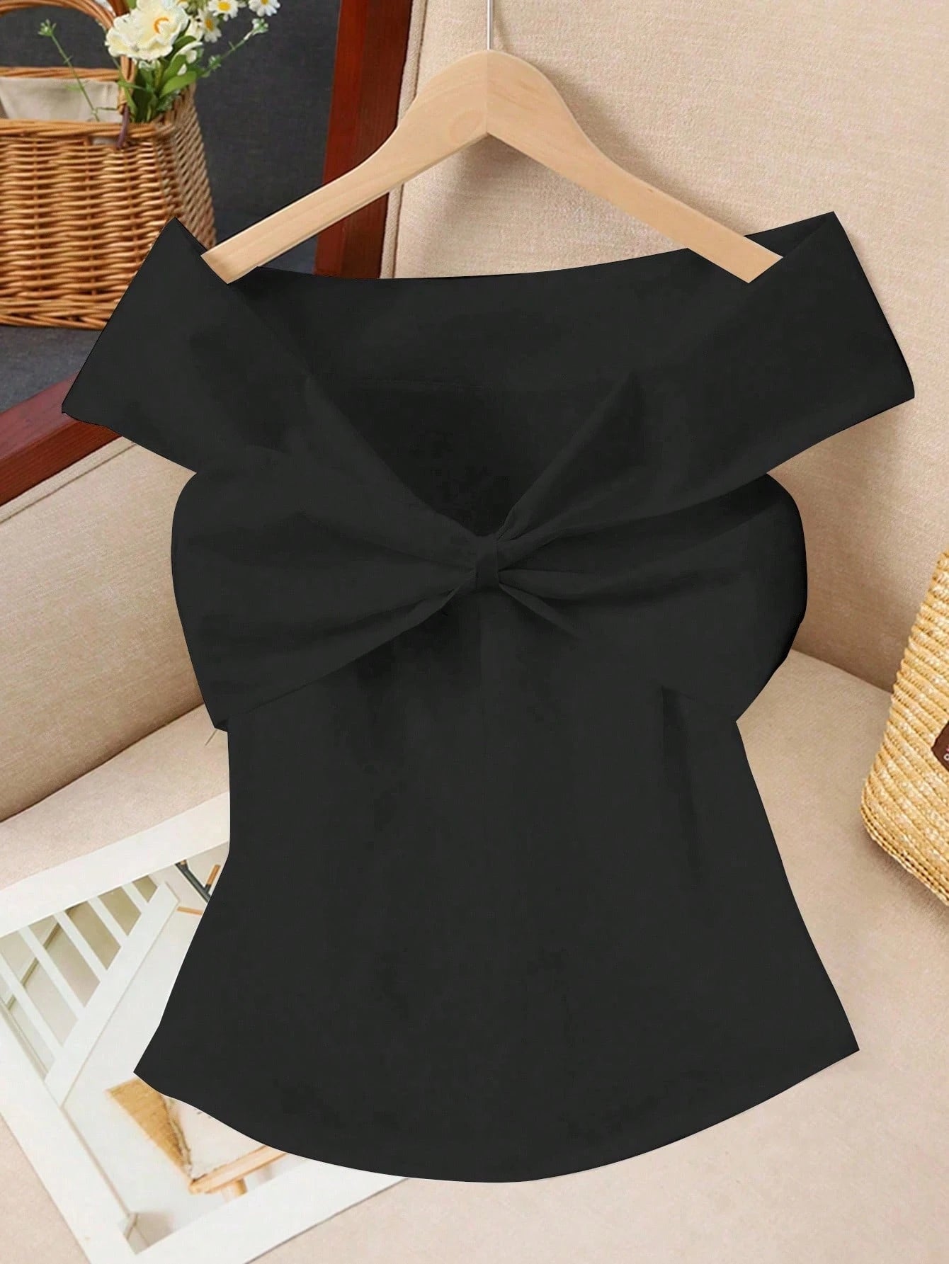 Black off-shoulder top with a large bow on a hanger against a neutral background