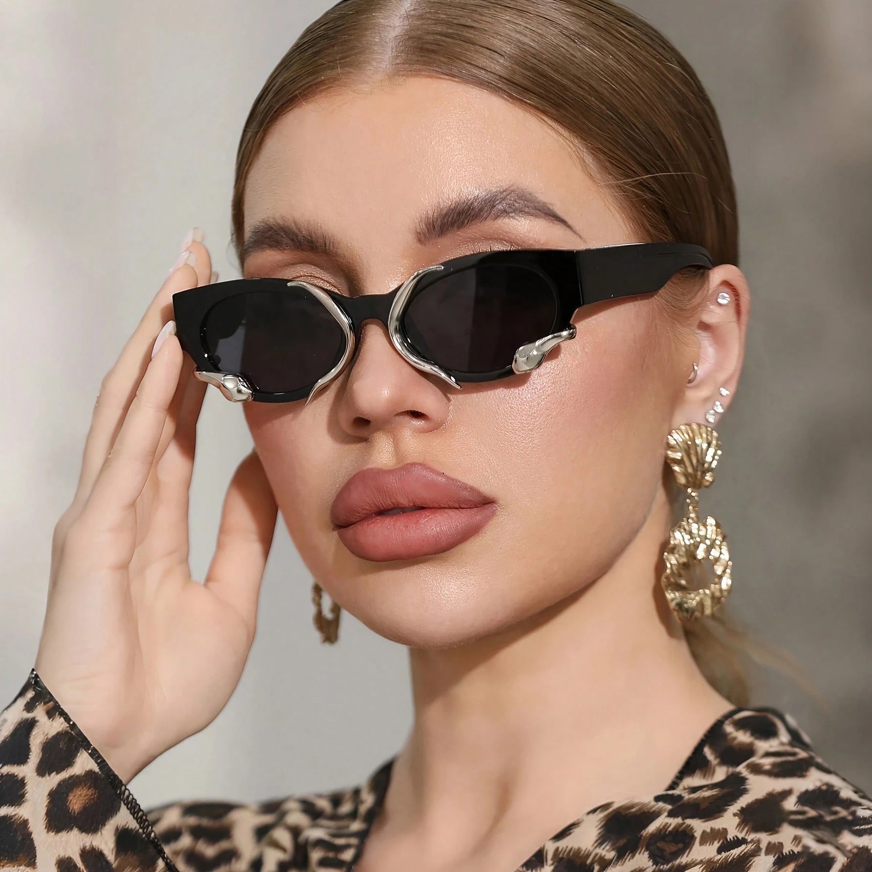Woman wearing stylish sunglasses and gold earrings with a neutral background