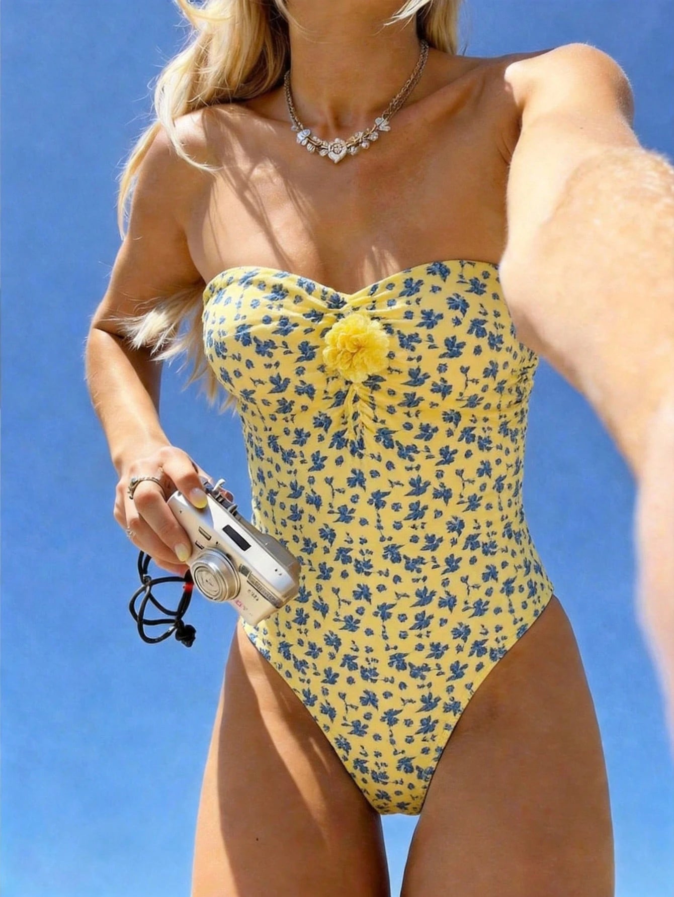 Woman wearing a yellow floral swimsuit against a clear blue sky.