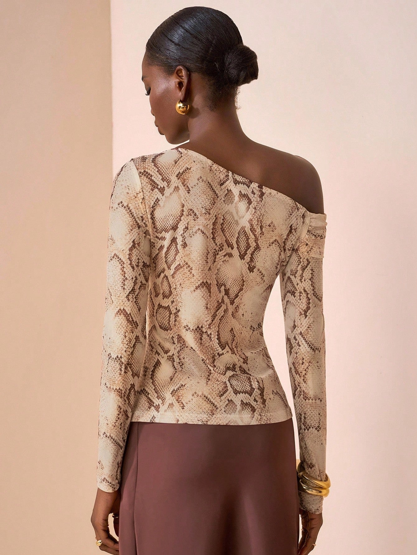 Woman wearing a snake print off-shoulder top with brown pants on a beige background