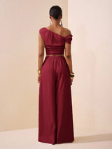 Person wearing a burgundy one-shoulder top and wide-leg pants against a beige background