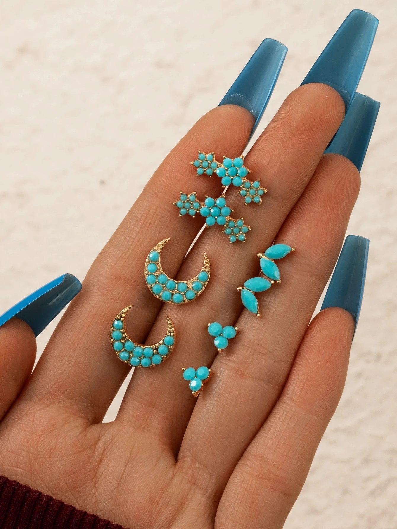 Turquoise earrings displayed on a hand with blue nail polish against a neutral background