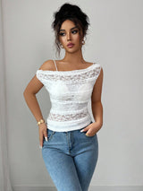 Woman wearing a white lace top and blue jeans against a plain background