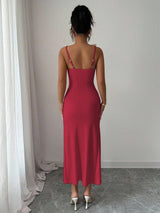 Woman wearing a red slip dress standing against a plain wall.