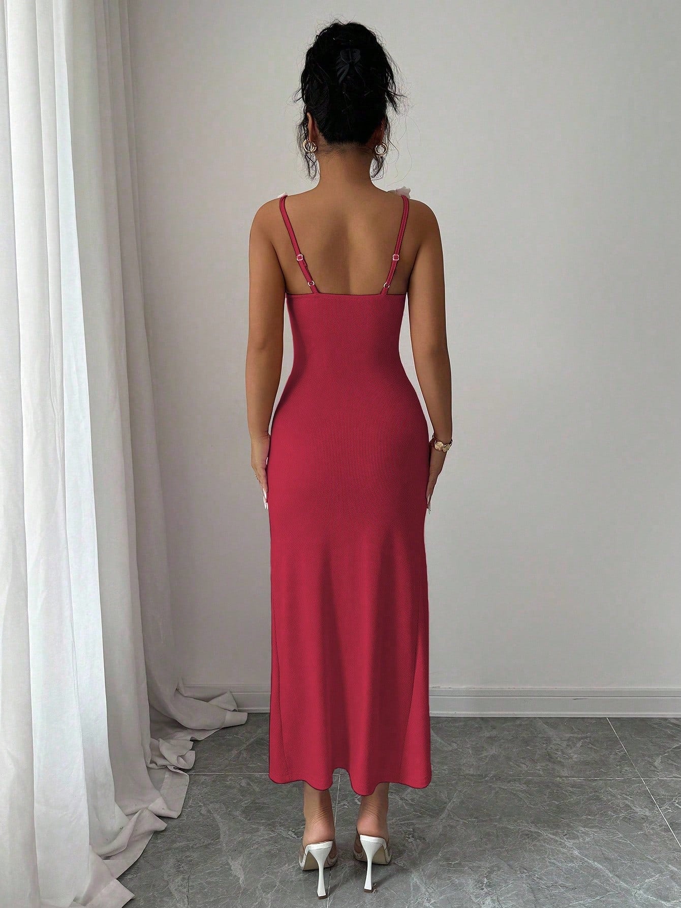 Woman wearing a red slip dress standing against a plain wall.