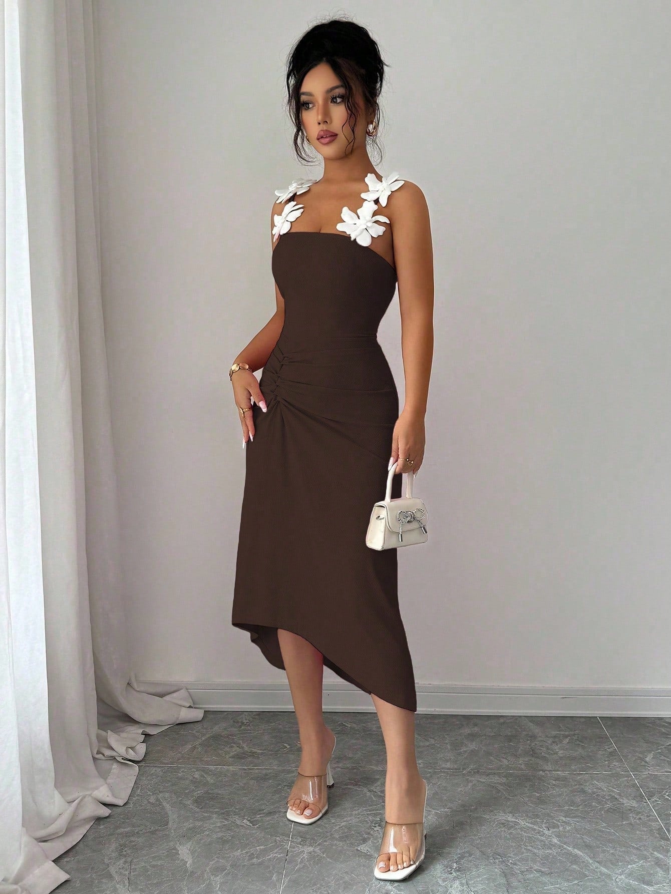 Woman wearing a brown dress with floral straps against a plain background