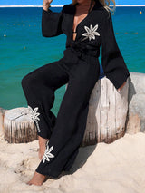 Person wearing a black outfit with white floral designs on a beach.