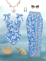 Blue and white patterned swimsuit with matching sarong, accessories on a light blue gradient background.