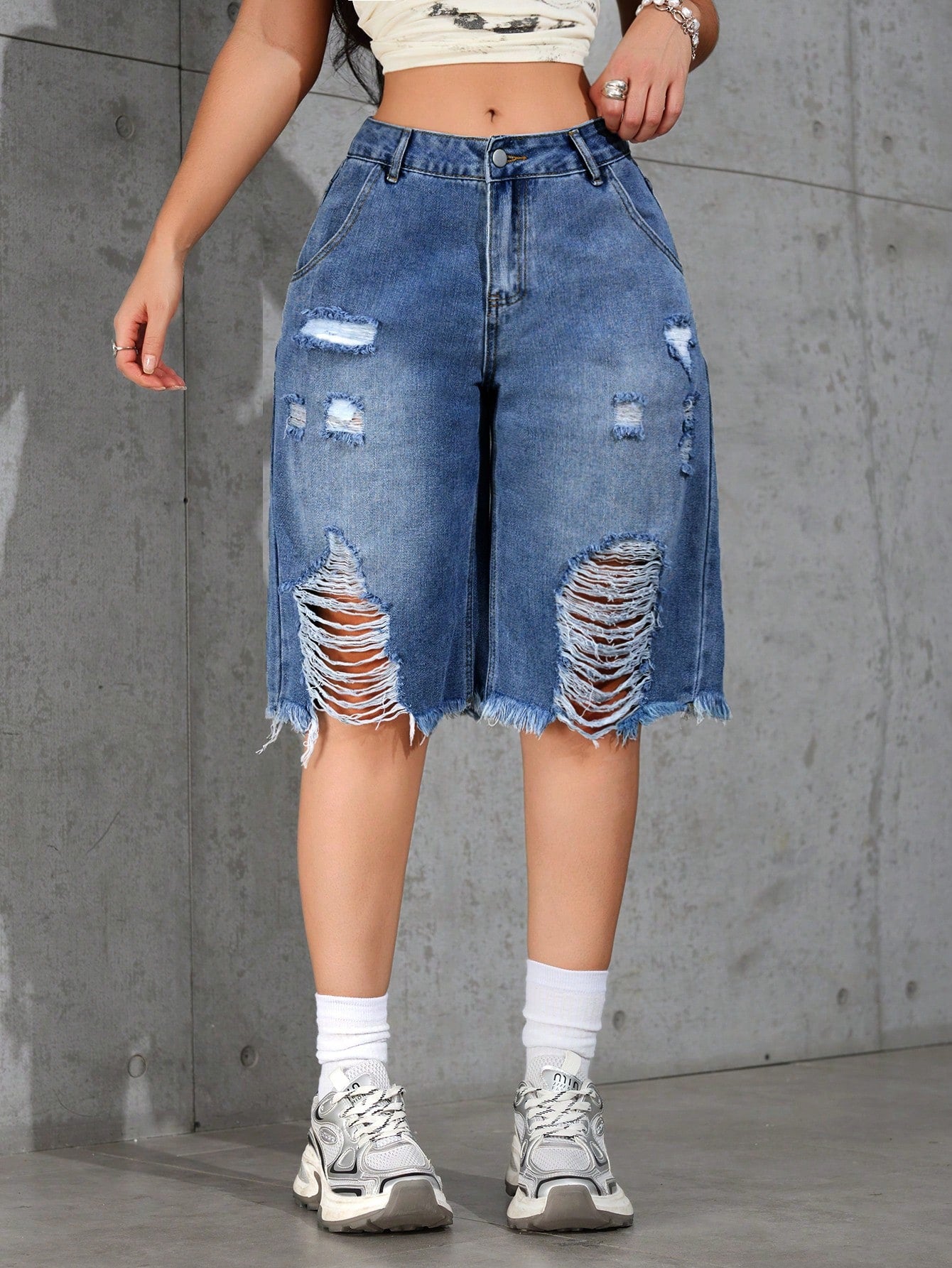Person wearing a distressed denim skirt against a gray concrete wall.